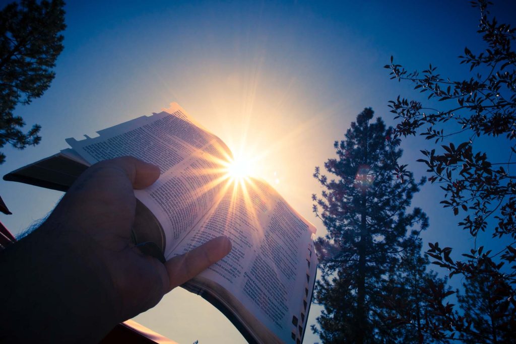 Open Bible Raised Skyward with Golden Sun Gleaming