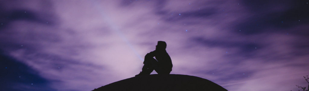 Shiloette of a Seated Man Contemplating a Night Sky and Faint Stars through Clouds